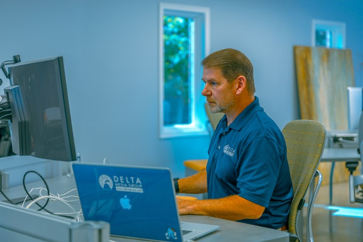 Delta Media Group owner Mike Minard working at a laptop and monitor in the company's office.