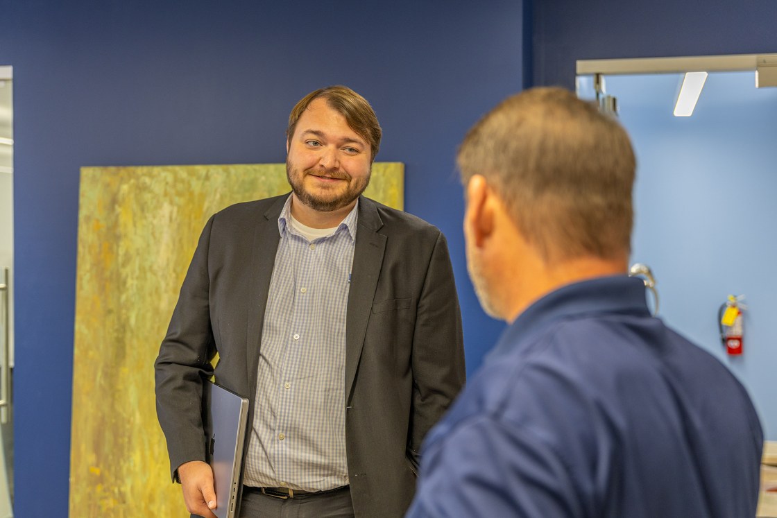 A Delta Media Group team member with a laptop talking with a colleague in the office.